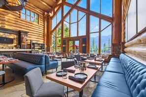A spacious indoor dining area with high ceilings and large windows, featuring wooden log walls, leather seating, and a stone floor. - Mountain Lodge Telluride (Telluride)