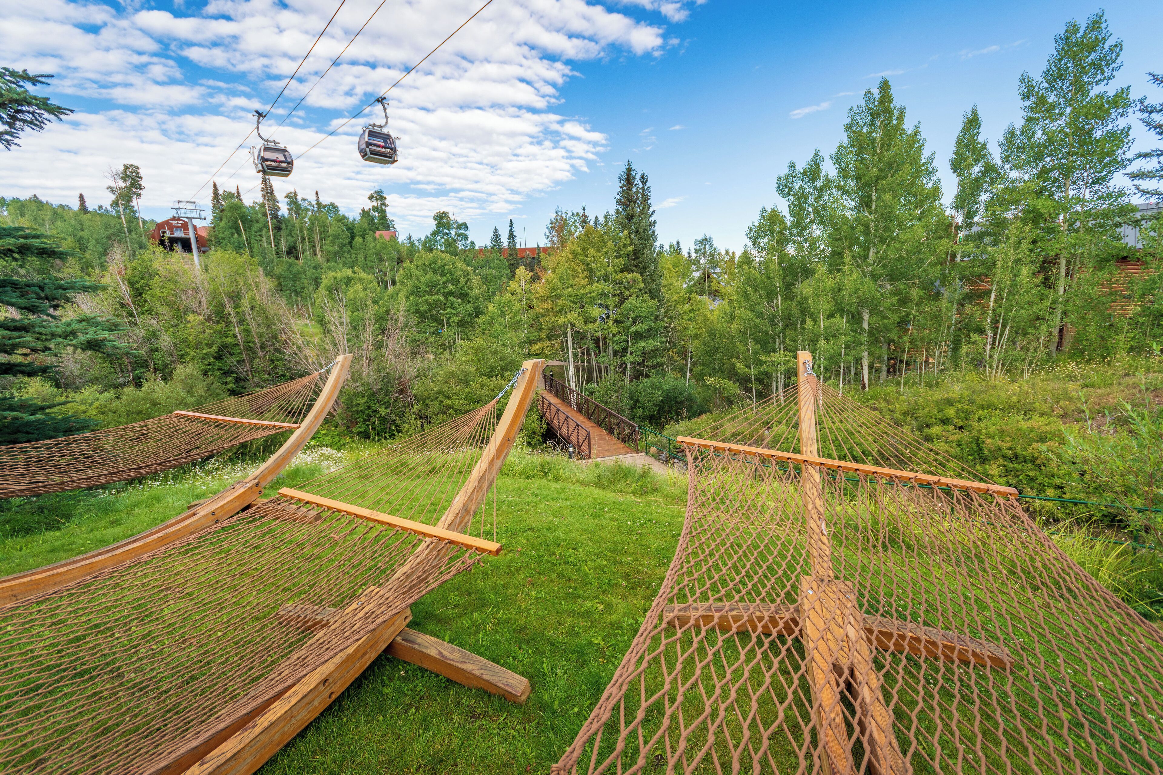 A hammock setup in a grassy area with a forest backdrop and a ski lift in the distance.