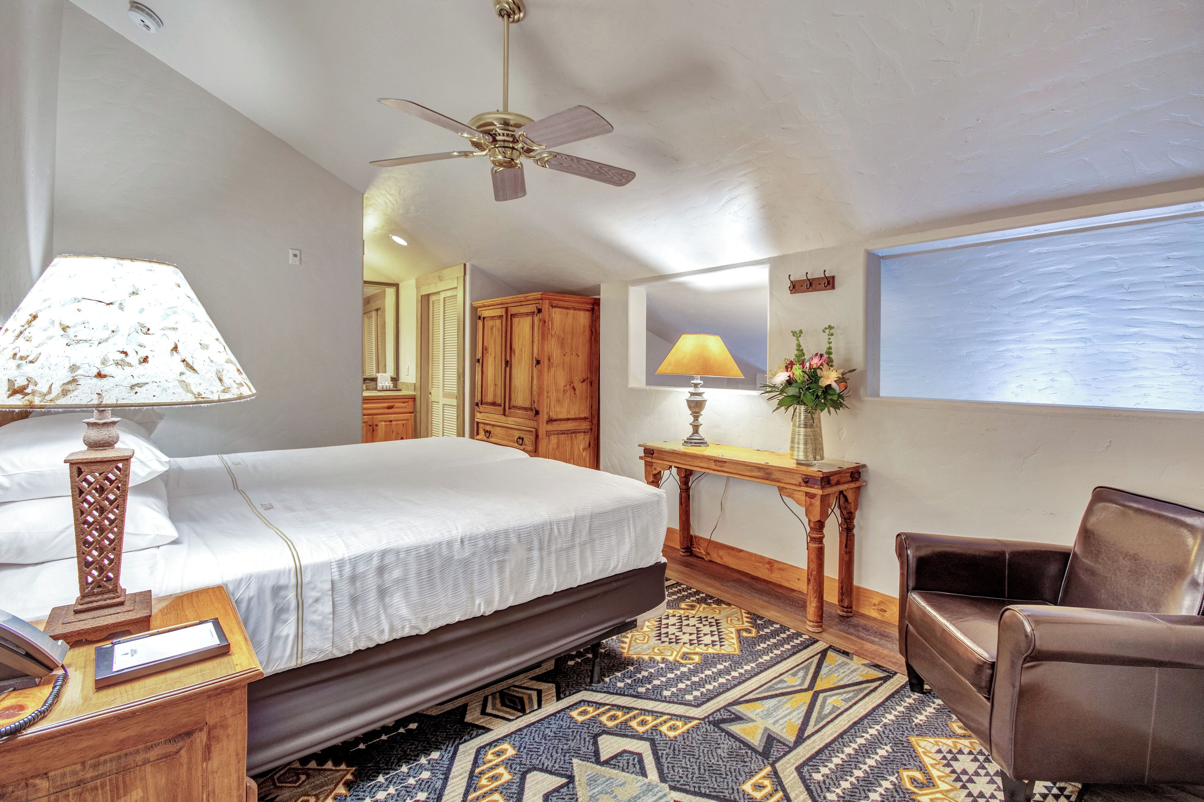 A bedroom with a bed, bedside table, lamp, wooden furniture, and a ceiling fan.