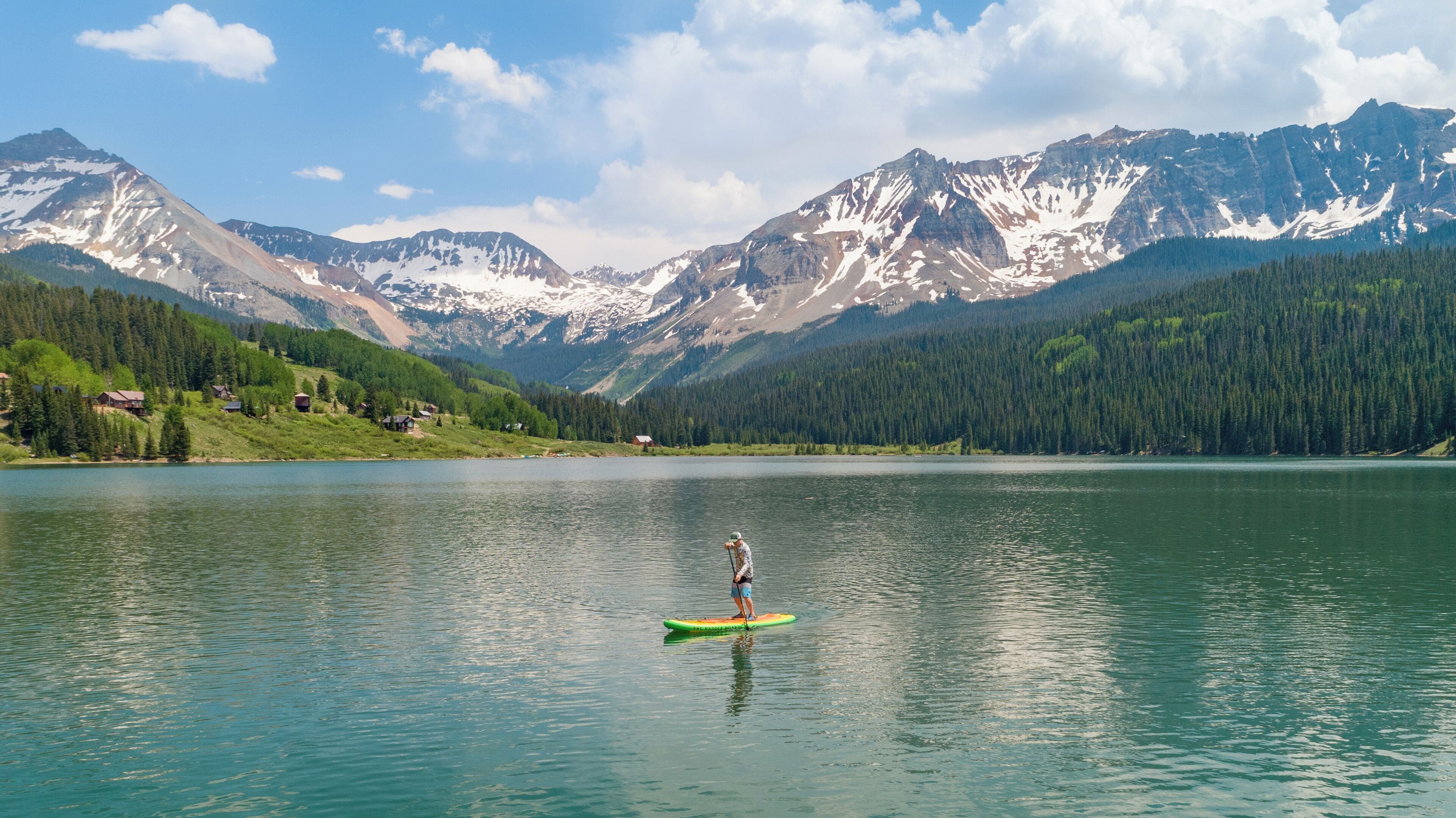 A person on a paddleboard in a calm lake with mountains in the background.