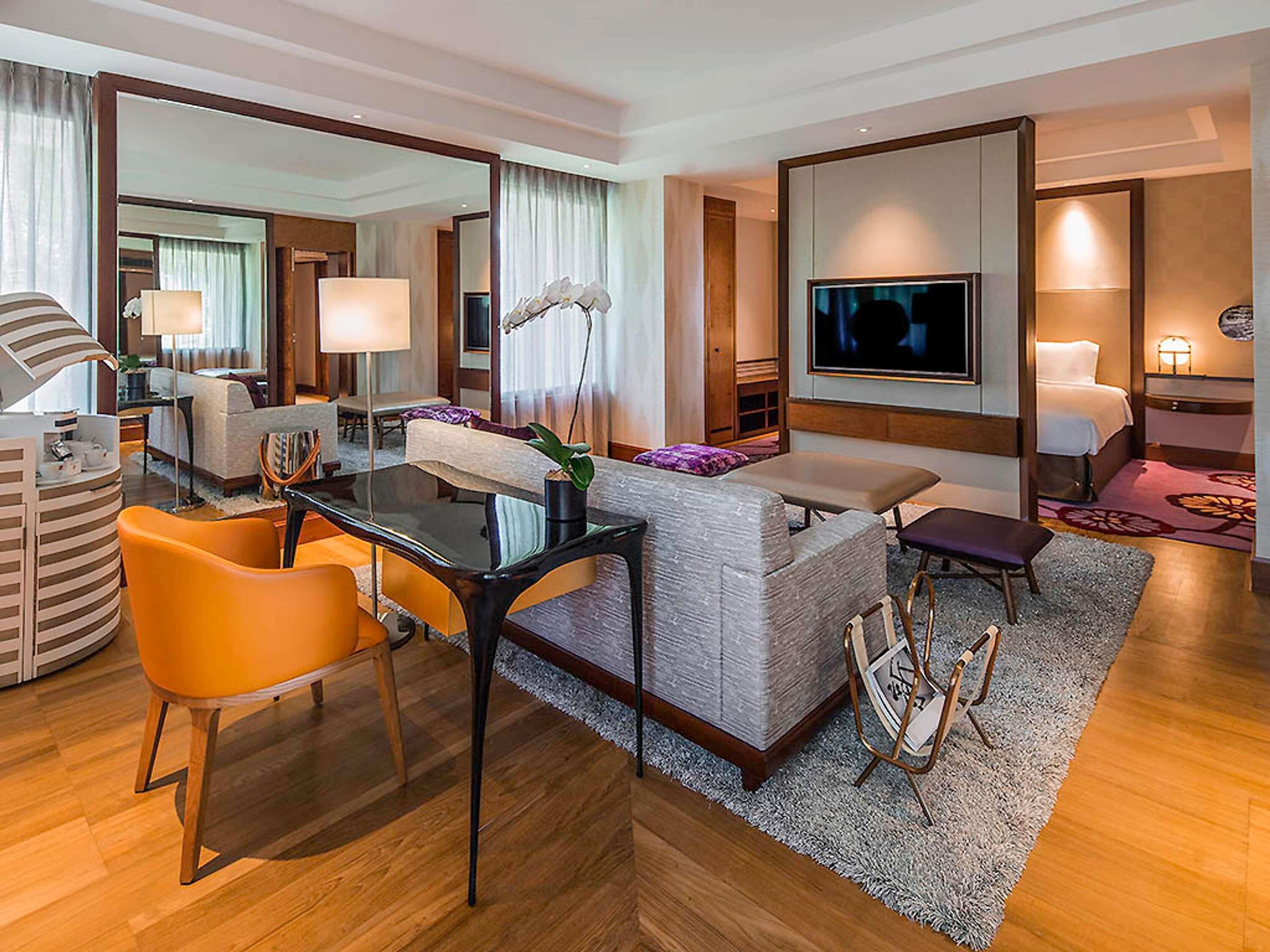 A hotel room with a dining area, a sofa, a TV, and a large mirror.