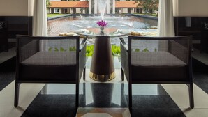 A room with a view of a pool and buildings, featuring two chairs, a table with a vase, and a large window with curtains. - Sofitel Singapore Sentosa (Singapore)