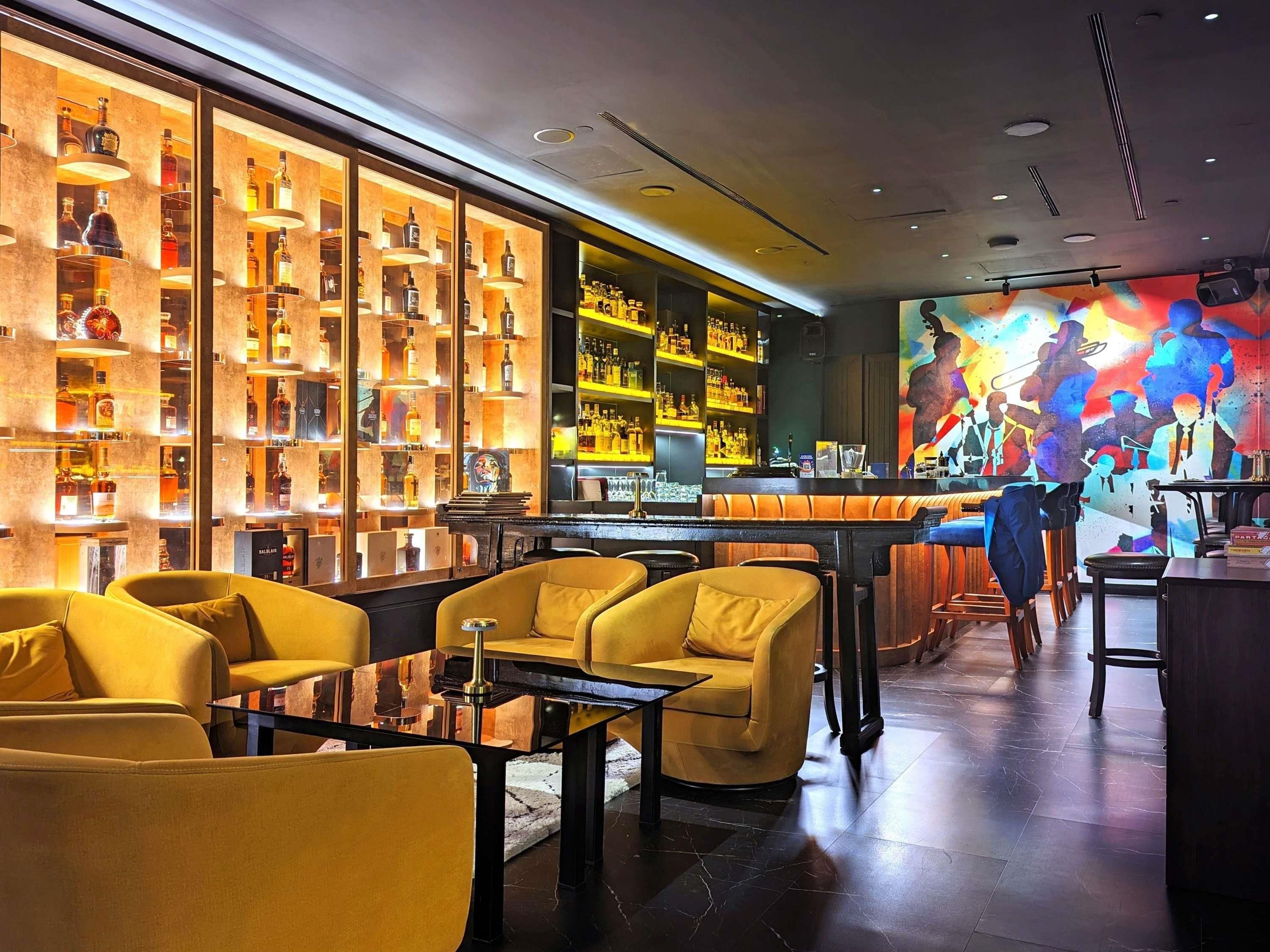 A bar area with yellow chairs, a piano, and shelves of liquor bottles.