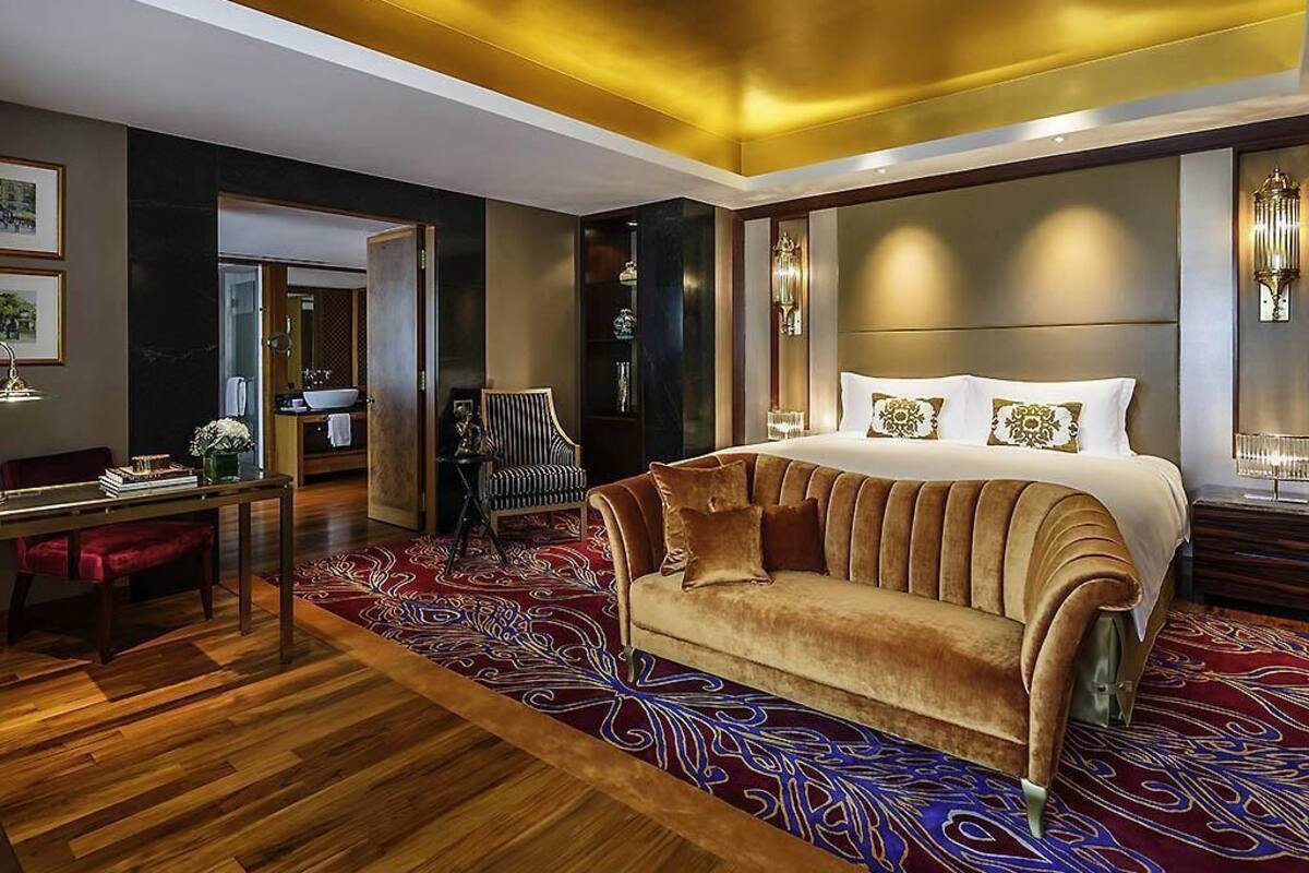A luxurious bedroom with a large bed, a sofa, a dining area, and a view of the outdoors.