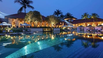 A hotel pool area with lounge chairs, umbrellas, and palm trees.