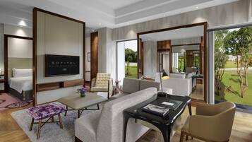 A modern hotel room with a sofa, armchair, and a TV on the wall.