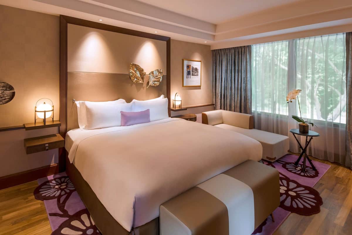 A hotel room with a large bed, a sofa, a small table with a plant, and a window with curtains.