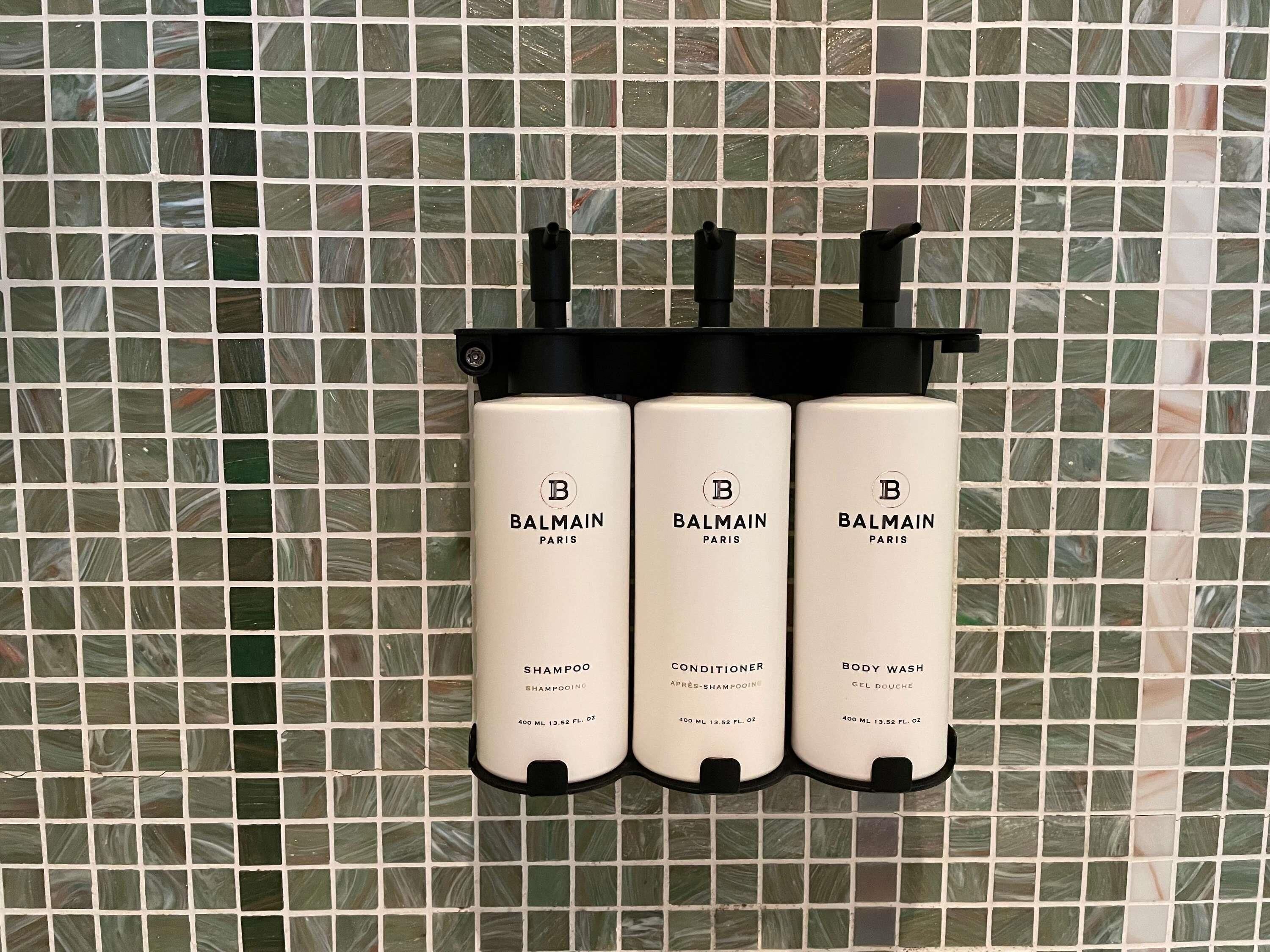 Three Balmain Paris products: shampoo, conditioner, and body wash, each in a black dispenser.