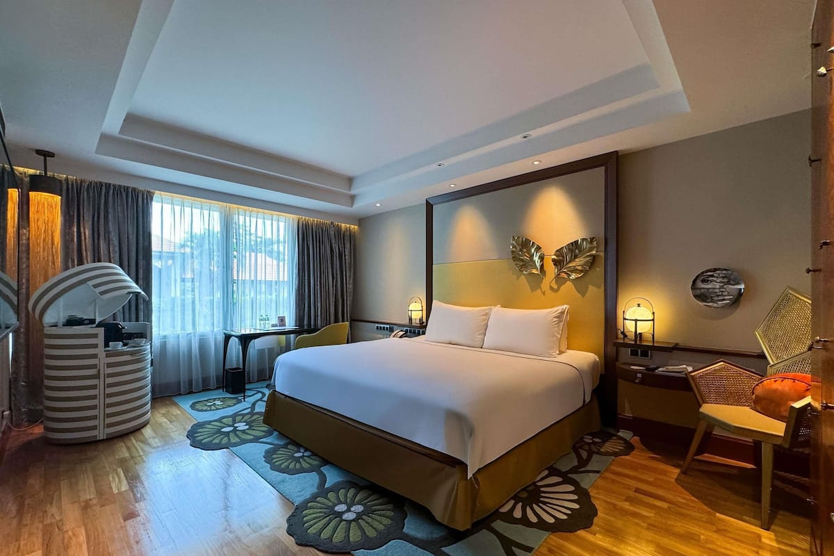 A hotel room with a large bed, a desk, a chair, a coffee machine, and a window with curtains.