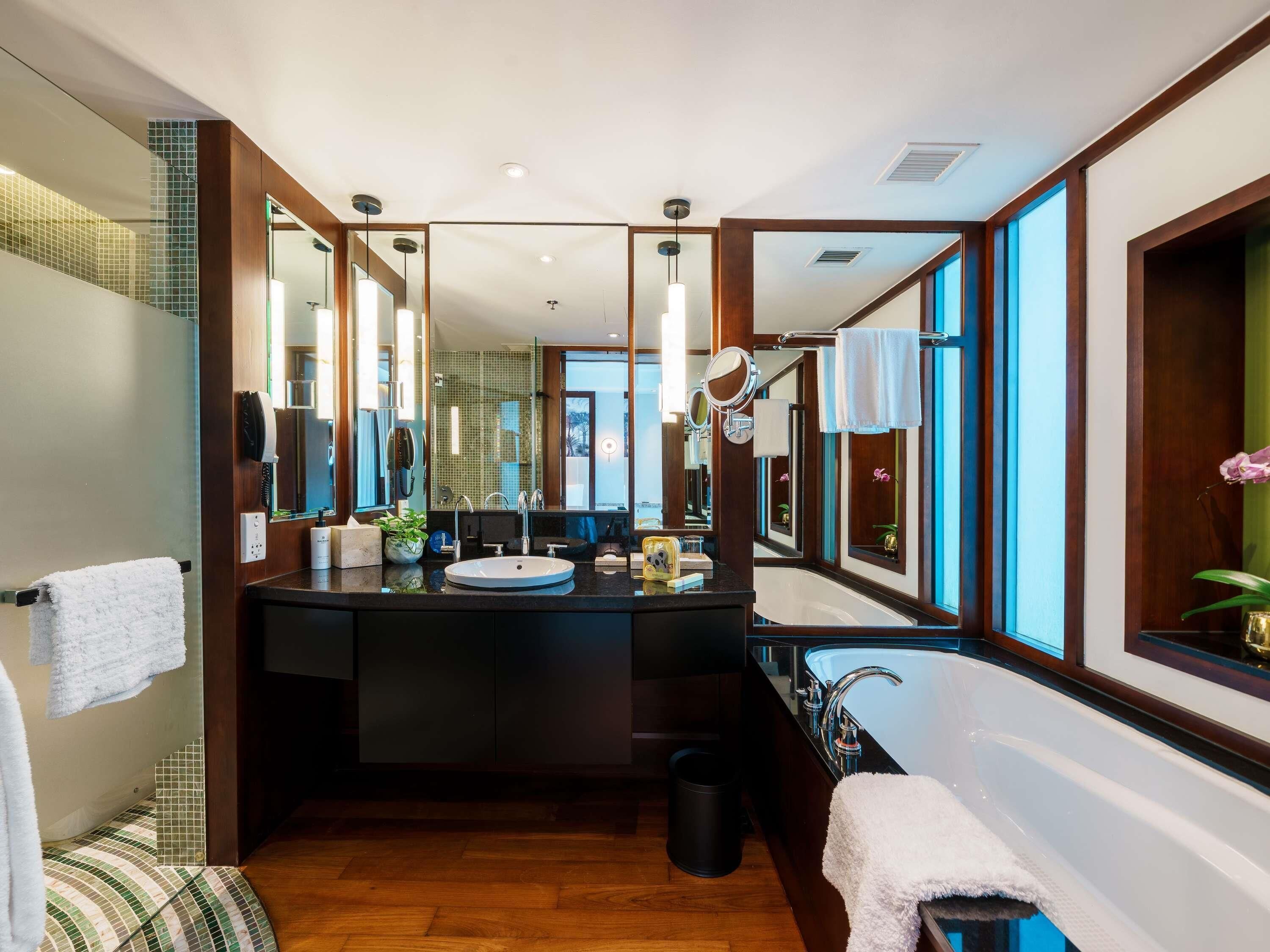 Une salle de bain moderne avec un grand miroir, un lavabo et une baignoire. On y trouve plusieurs miroirs et une coiffeuse avec un miroir au-dessus du lavabo.