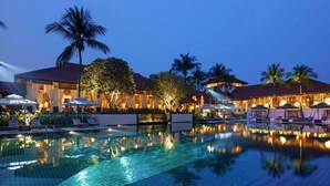 A swimming pool with lounge chairs and umbrellas, surrounded by palm trees and buildings with warm lighting. - Sofitel Singapore Sentosa (Singapore)