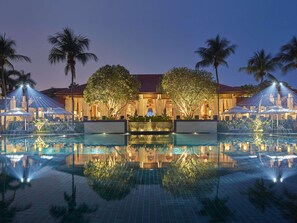 A pool area with a reflection, palm trees, and a building with a red roof. - Sofitel Singapore Sentosa (Singapore)