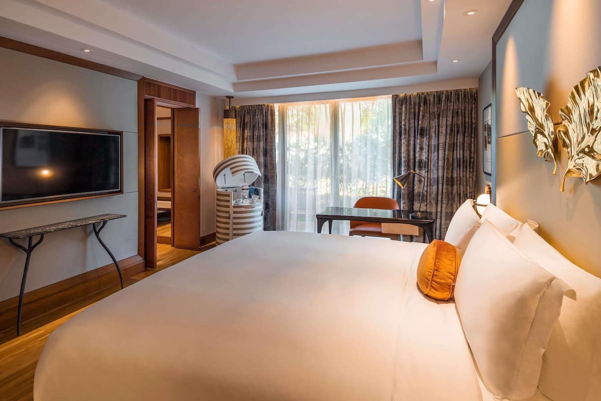 A hotel room with a large bed, a TV, a desk with a chair, a lamp, and a window with curtains.