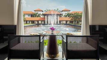 A view from a room with two chairs facing a fountain and a pool, with buildings in the background.