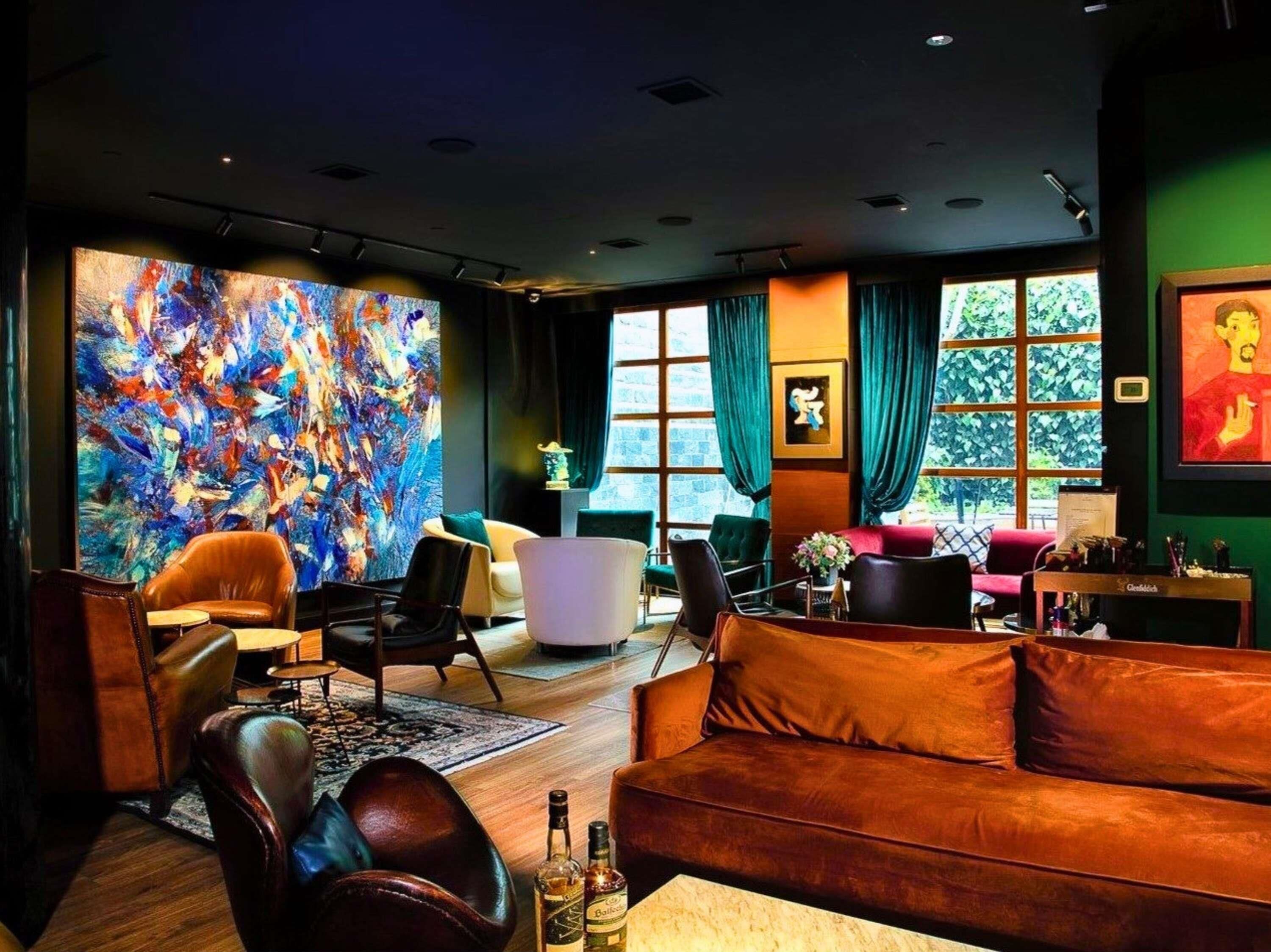 A modern living room with a large abstract painting, leather sofas, and a view of greenery through large windows.