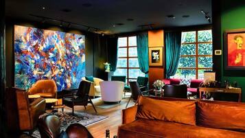 A modern living room with a large abstract painting, leather sofas, and a view of greenery through large windows.