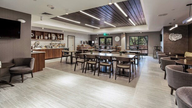 A spacious restaurant with multiple dining tables and chairs, a kitchen area, and a modern ceiling design.