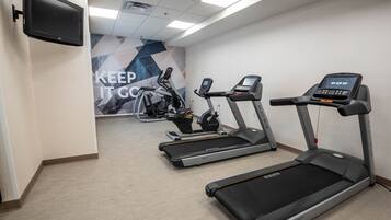 Une salle de sport équipée de tapis de course, de vélos d’appartement et d’un téléviseur fixé au mur.