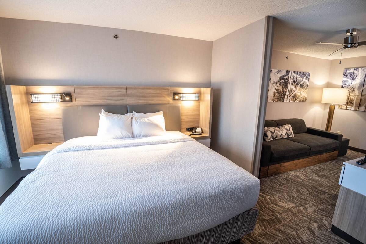 Een hotelkamer met een groot bed, nachtlampjes, een bank en kunst aan de muren.