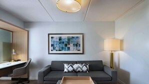 Ein modernes Wohnzimmer mit einem grauen Sofa, einem Holztisch, einem Schreibtisch mit Stuhl, einem gerahmten abstrakten Kunstwerk und einer Stehlampe.