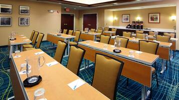 A hotel conference room with multiple tables, chairs, and a coffee station.