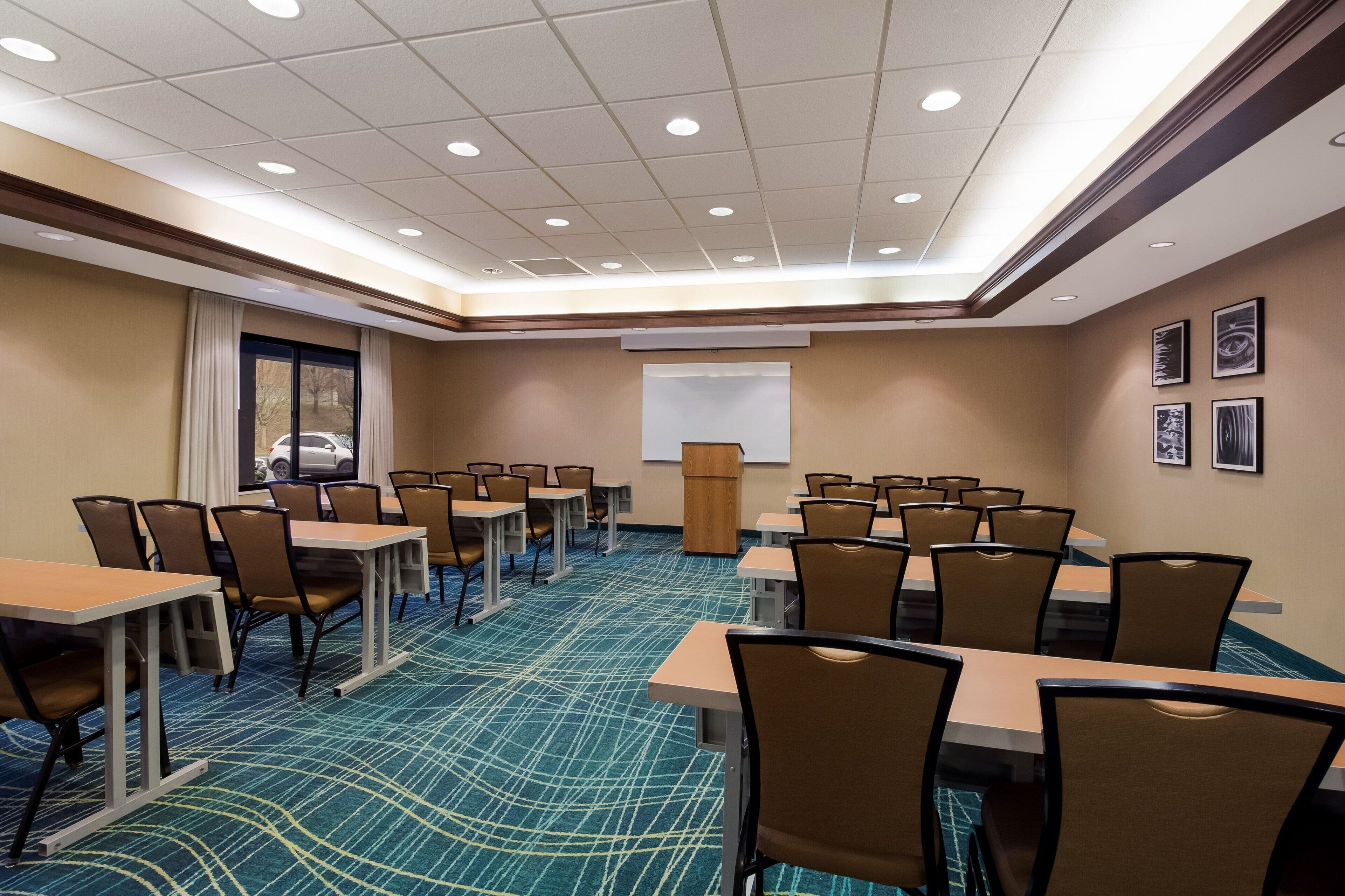 A conference room with multiple tables and chairs, a projector screen, and a large window with curtains.