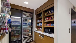 Eine Küchenzeile mit Kühlschrank, Mikrowelle und Regalen voller Snacks und Getränke.