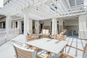 Een terras buiten met witte meubels, waaronder tafels en stoelen, onder een witte pergola.
