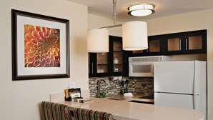 A modern kitchen with a white refrigerator, a microwave, and a sink. There is a striped chair and a framed picture on the wall. - Sonesta ES Suites San Antonio Northwest - Medical Center (San Antonio)