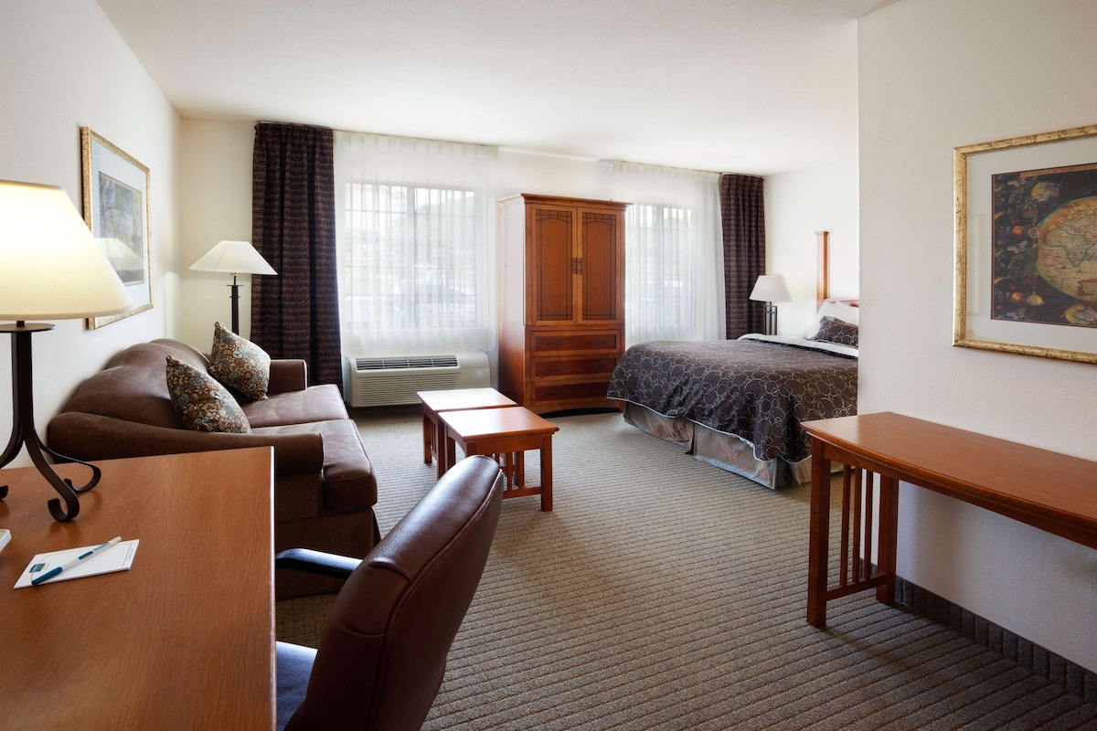 A hotel room with a bed, a desk, a chair, a sofa, a wardrobe, and a lamp.