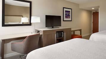 Una habitación de hotel con una cama, un escritorio con televisor, una silla, una lámpara y un cuadro en la pared.