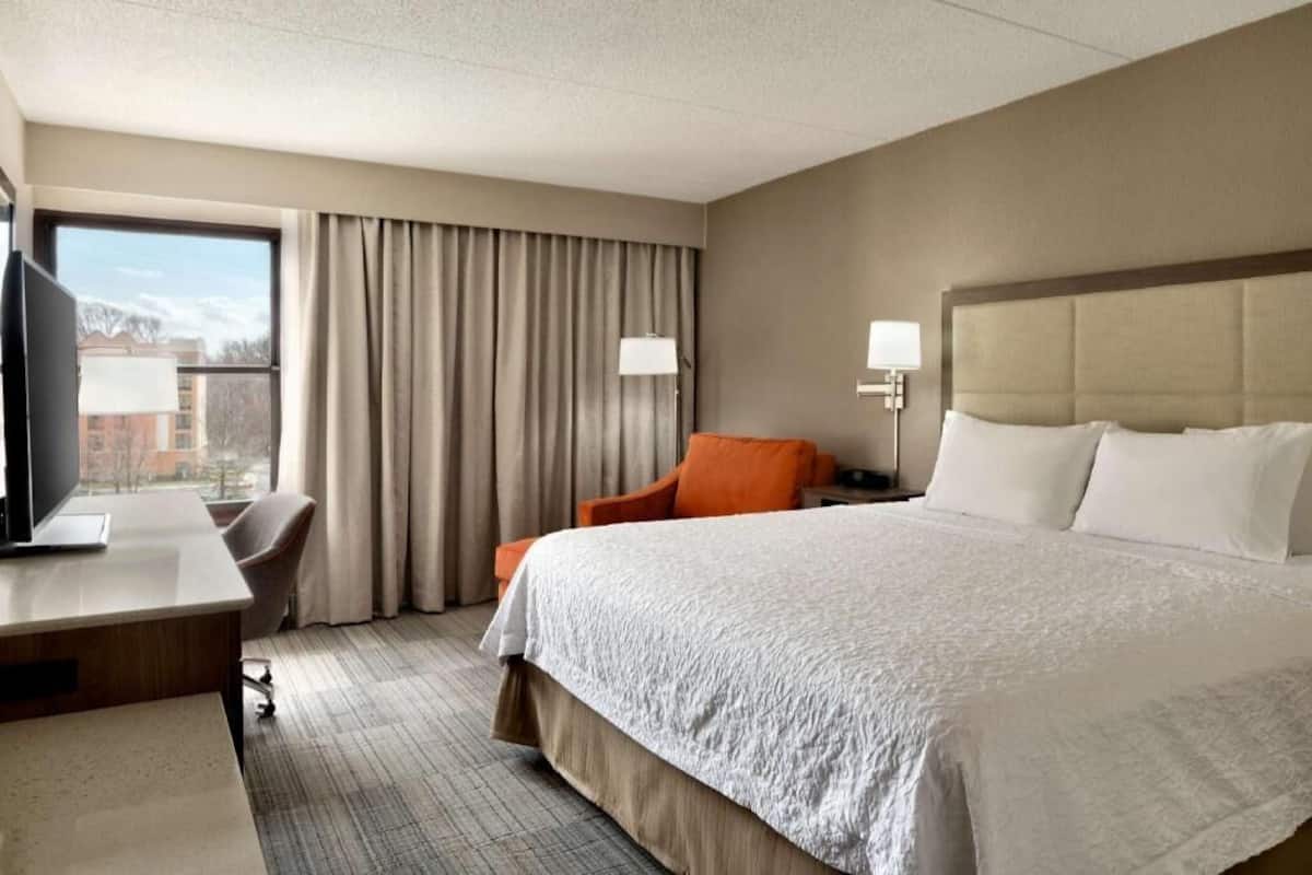 A hotel room with a bed, a desk, a chair, a TV, and a window with curtains.