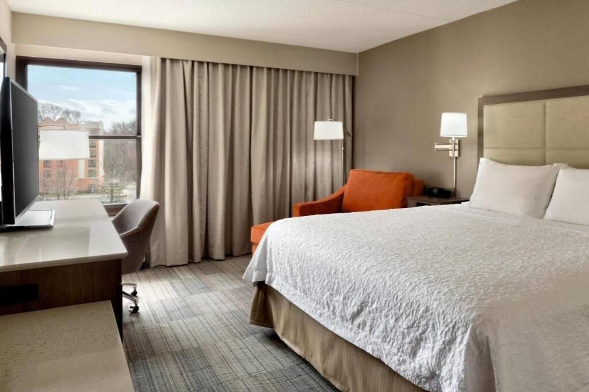 A hotel room with a bed, desk, chair, and a TV.