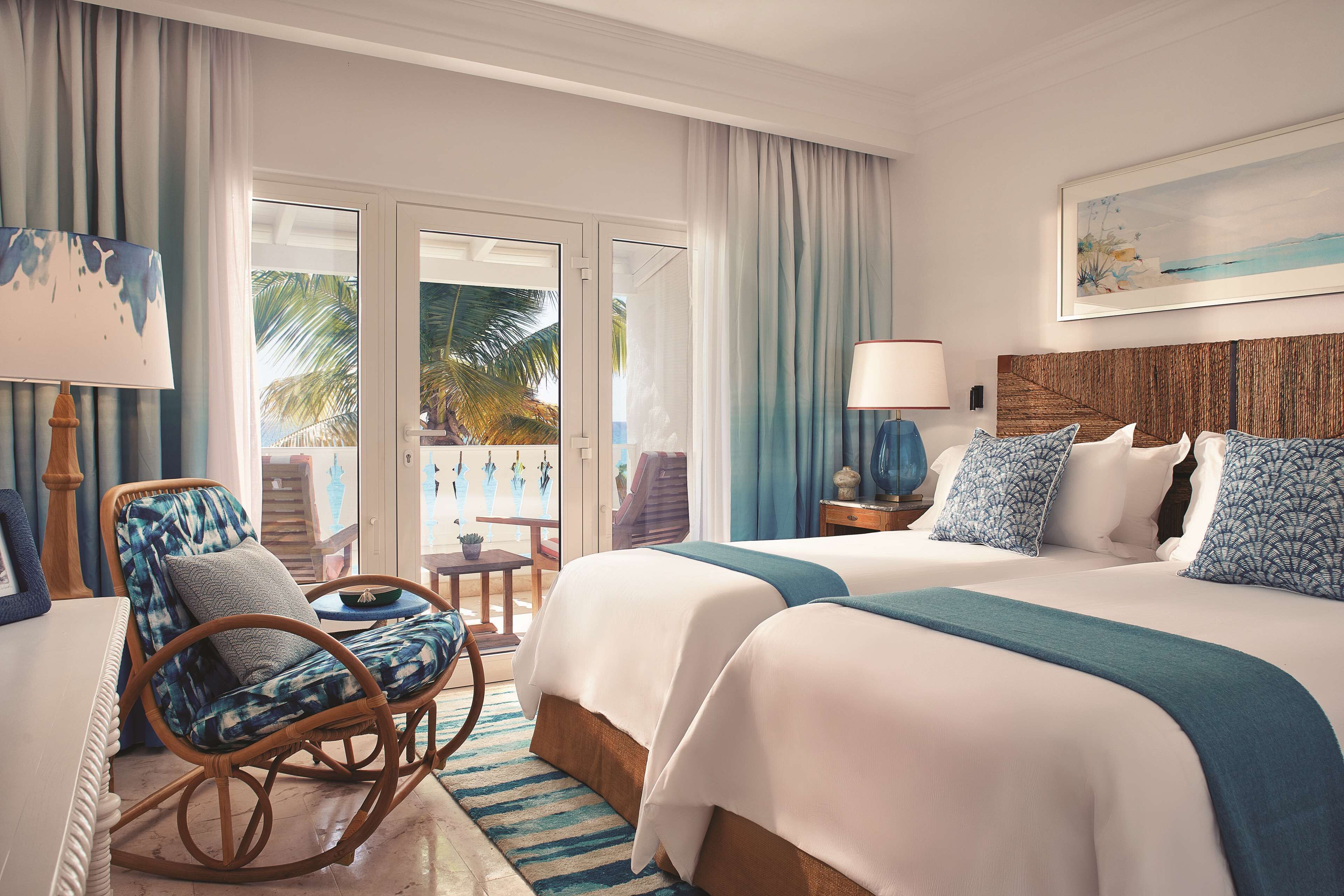 Habitación de hotel con cama, una silla, una mesa y vistas a palmeras a través de la puerta de cristal.