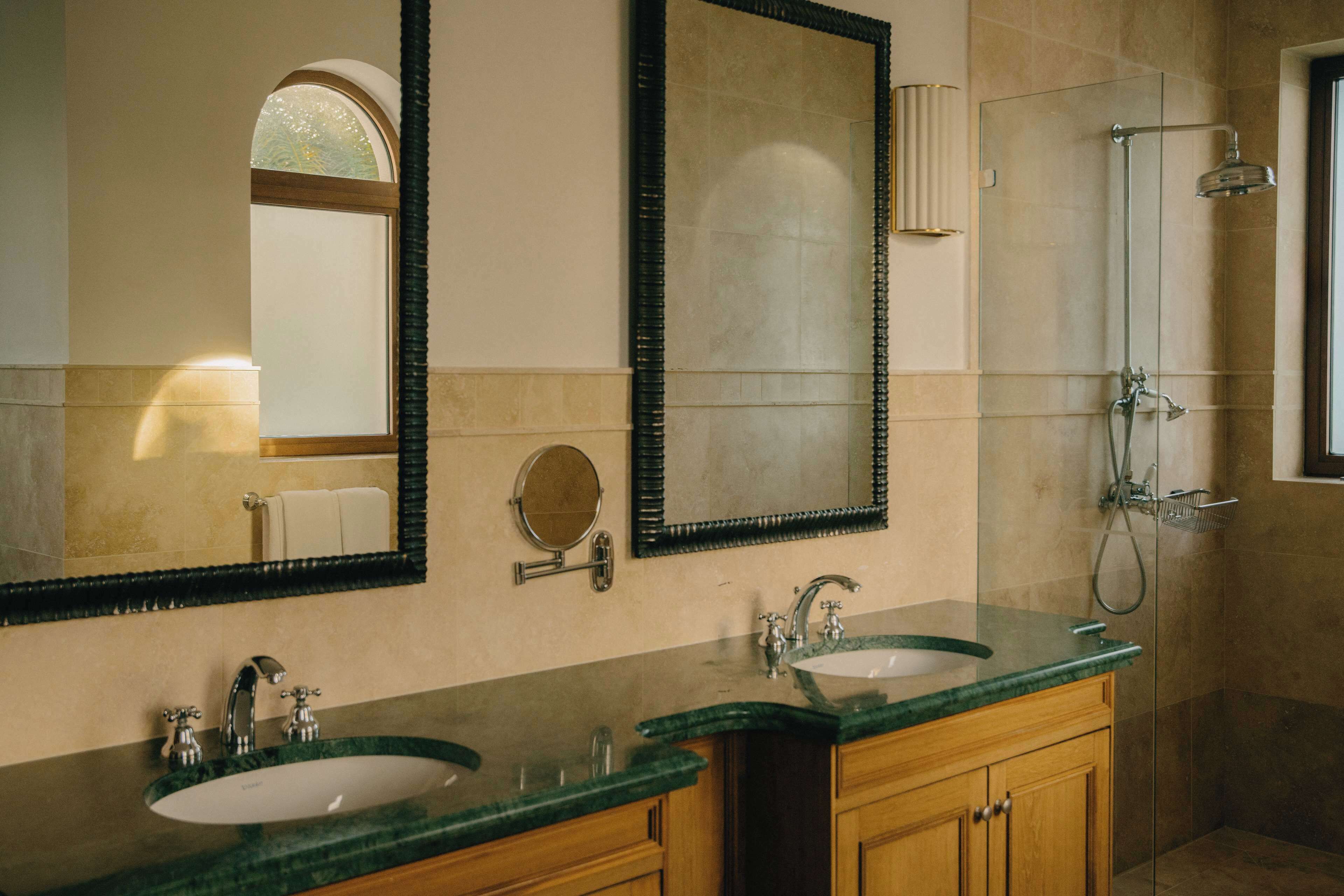 A bathroom with two sinks, a large mirror, a shower, and a towel rack.