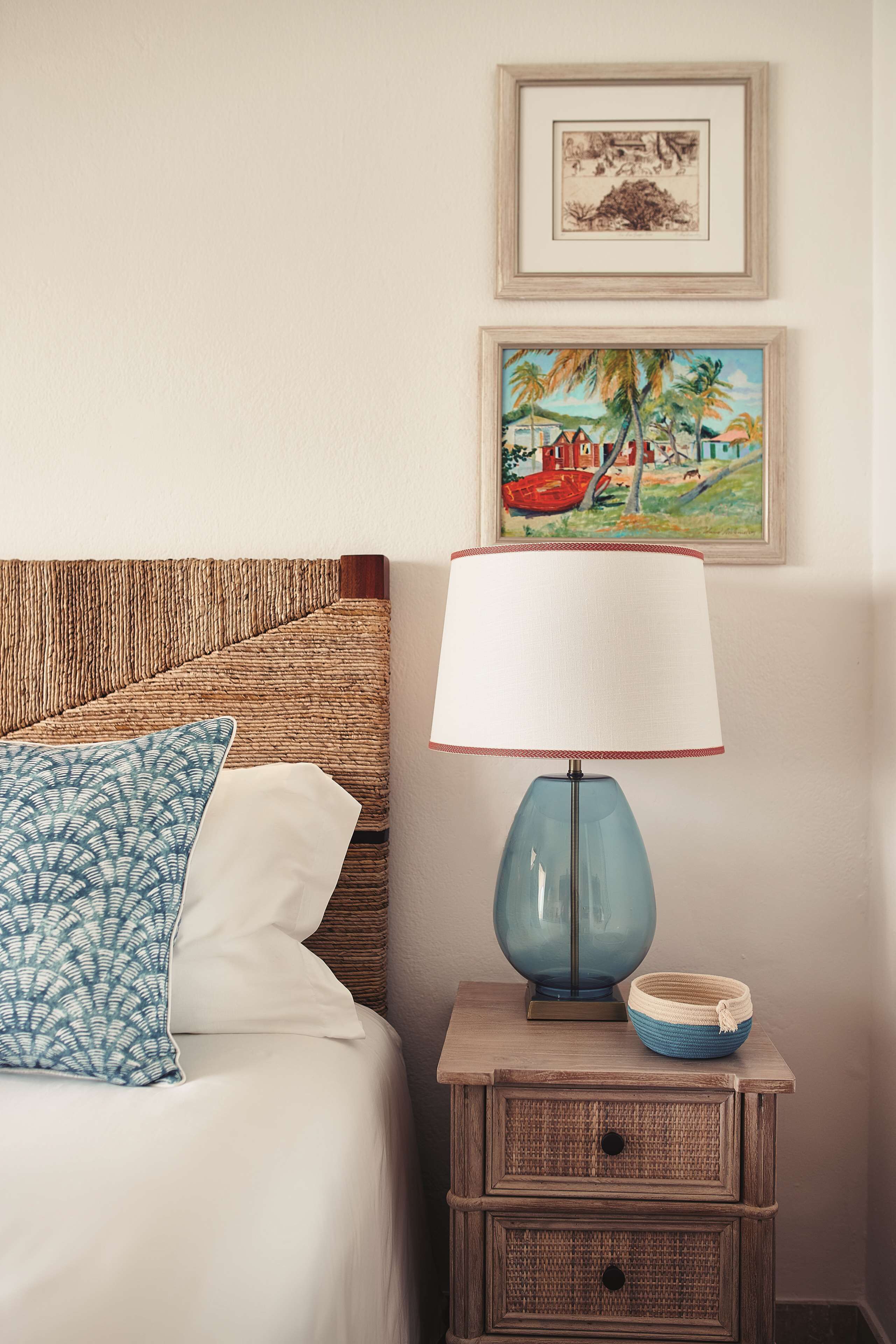 A neatly made bed with a blue patterned pillow, a blue lamp on a bedside table, and two framed artworks on the wall.