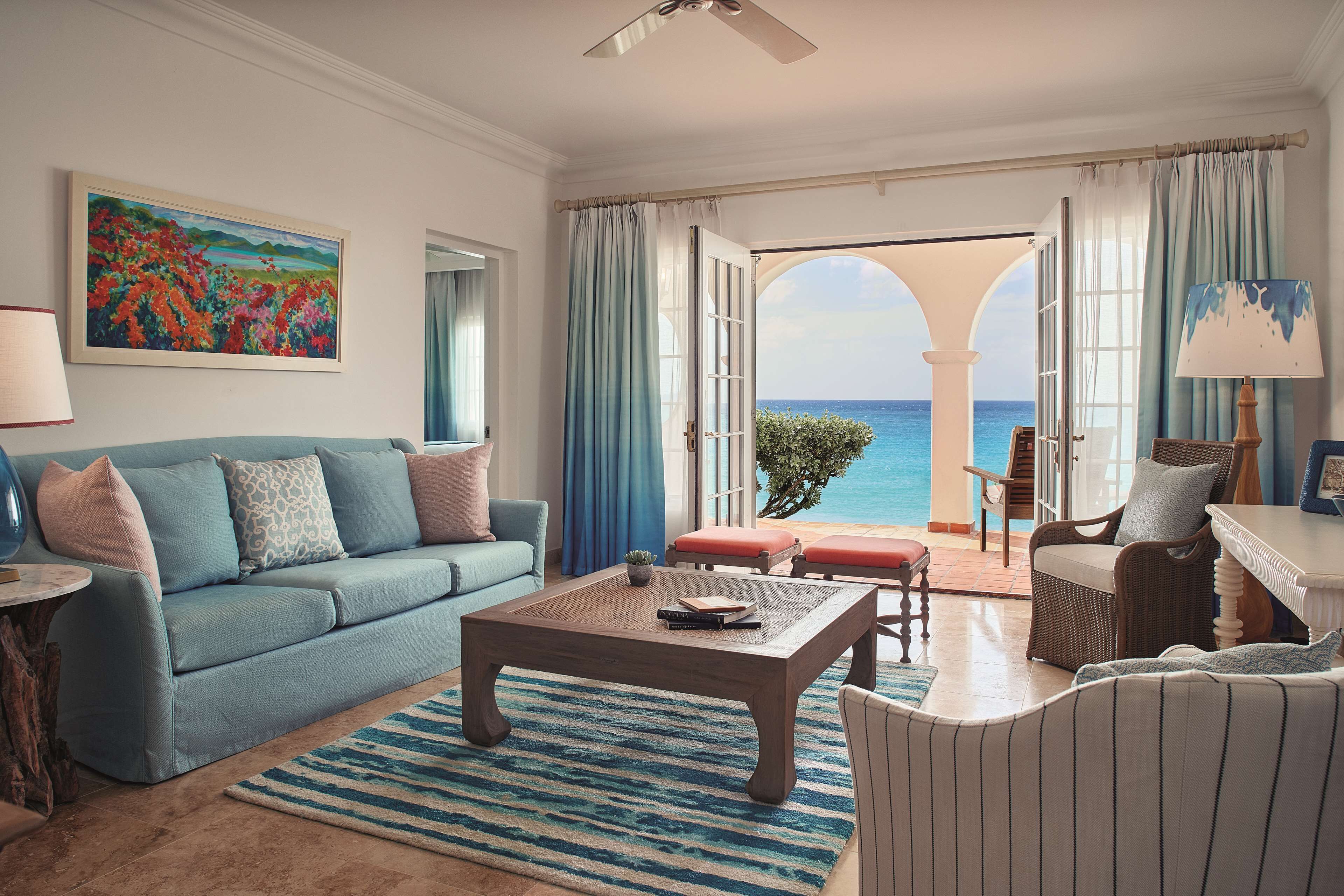A living room with a view of the ocean, a blue sofa, a coffee table, and a wicker chair.