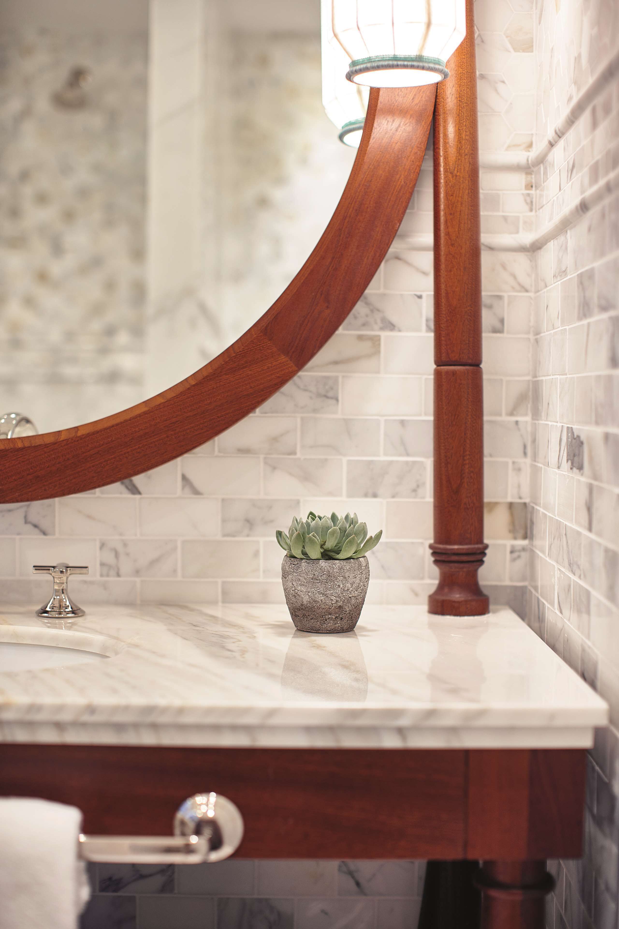 Une salle de bain avec un comptoir en marbre, un miroir en bois aux lignes courbes, une plante en pot et un porte-serviettes.