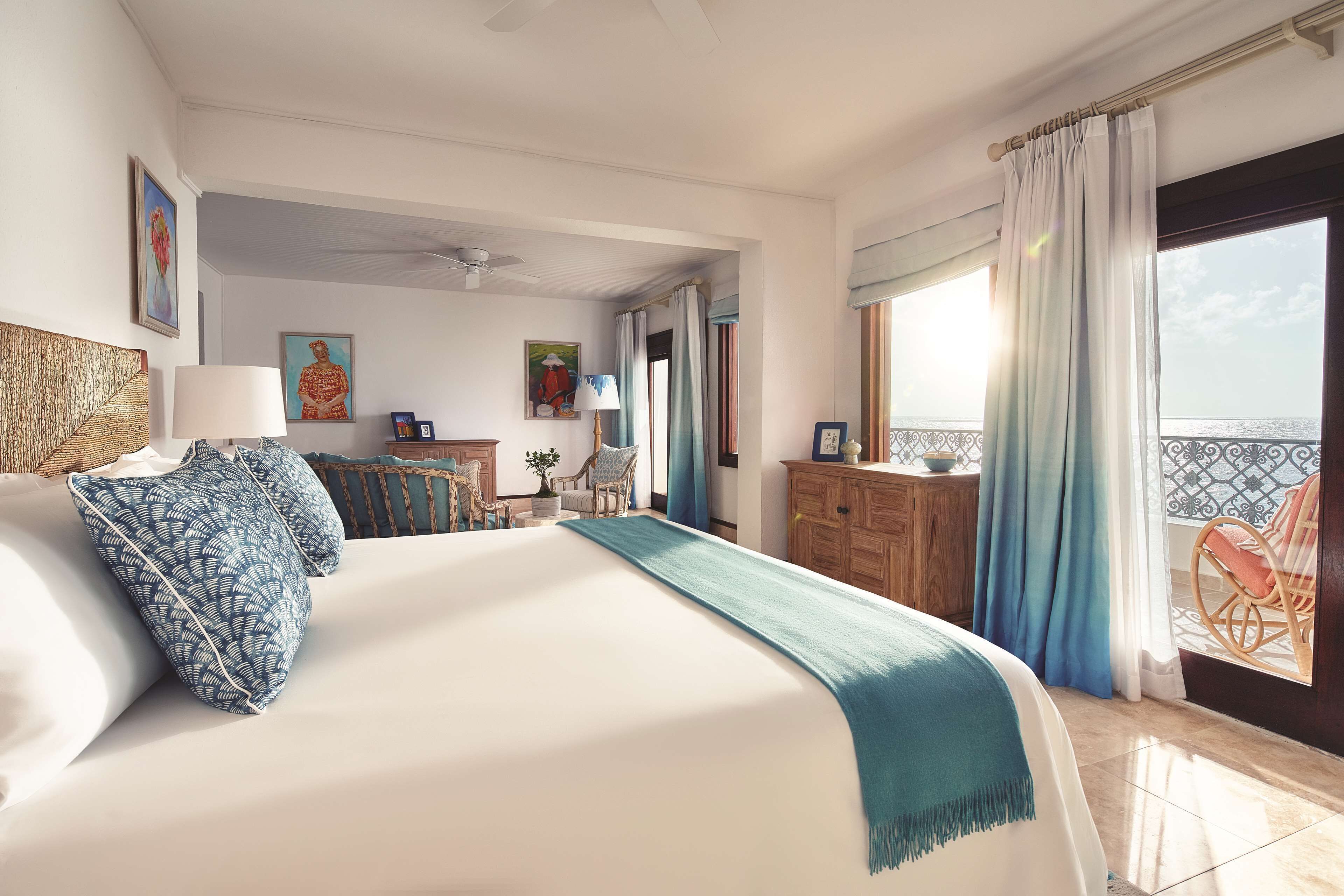 A hotel room with a large bed, a wooden dresser, a chair, and a balcony with a view.
