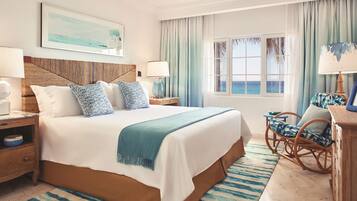 A hotel room with a large bed, two bedside tables, a chair, a view of the ocean, and a ceiling fan.