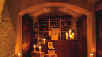 Experience the wine cellar's intimate atmosphere, featuring a collection of wine bottles on wooden shelves and a warm glow from lit candles.