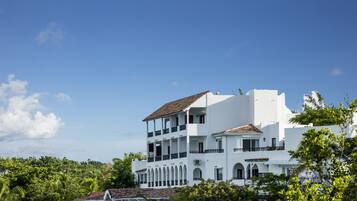 A white multi-story building with balconies, surrounded by lush greenery.