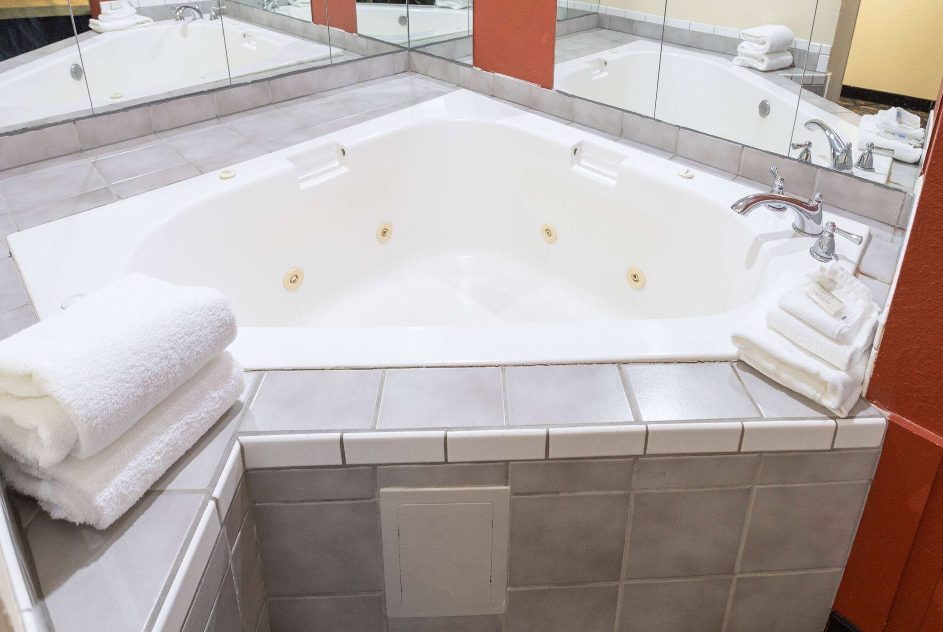 A large, rectangular bathtub with a single faucet and a control knob, surrounded by a tiled wall and a mirror.