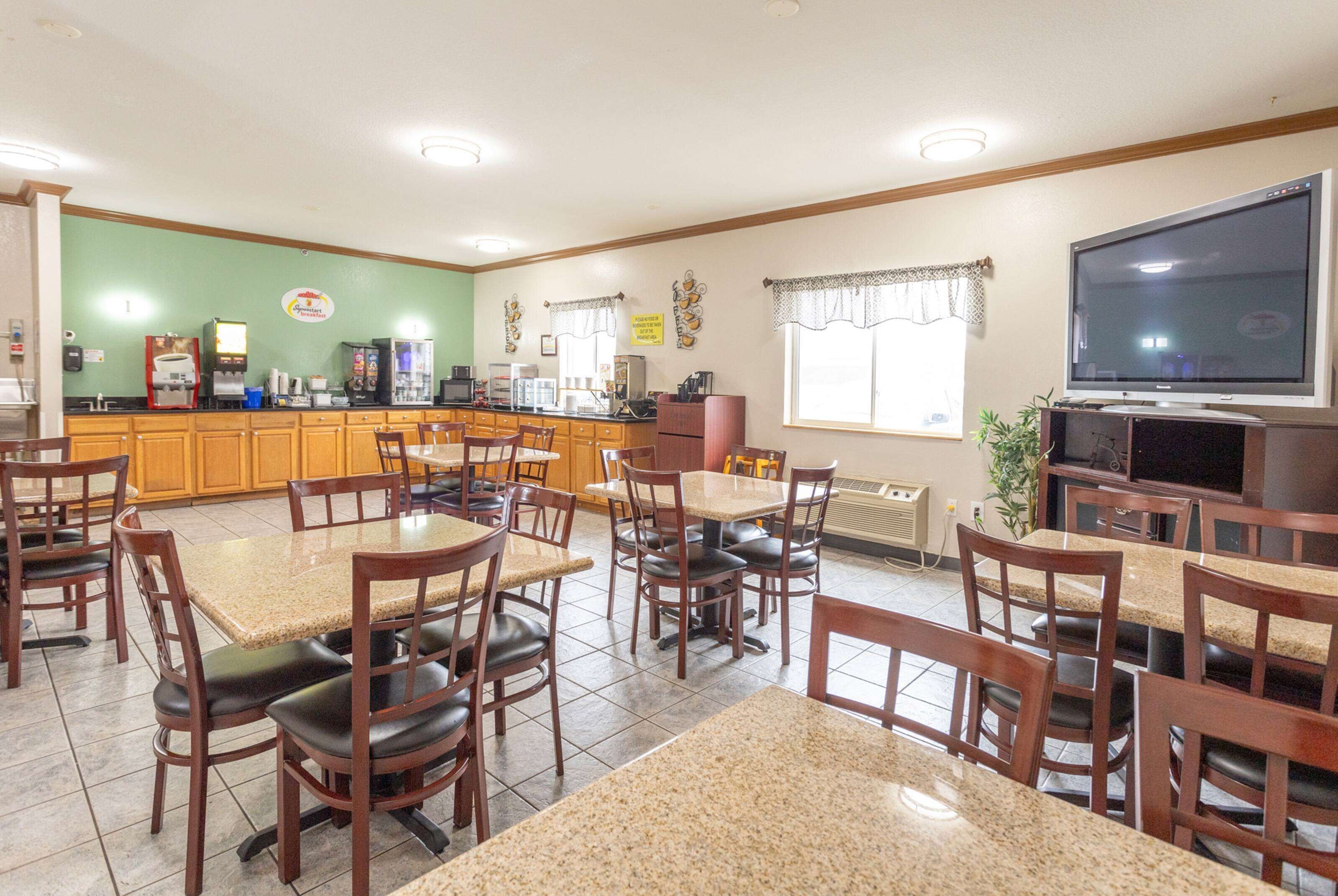 A dining area with multiple tables and chairs, a kitchen area with appliances, and a television on the wall.