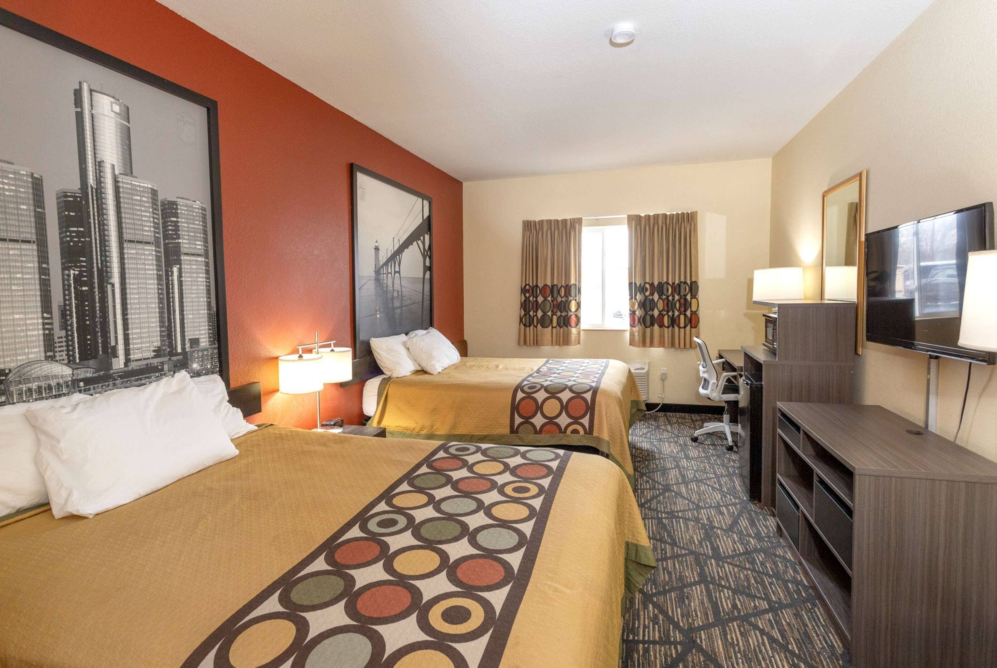 Habitación de hotel con dos camas, un escritorio, televisor y ventana con cortinas.
