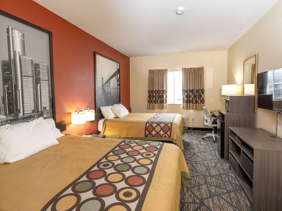 A hotel room with two beds, a desk, a TV, and a window with curtains.