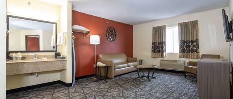 A hotel room with a bathroom, a sofa, a small table, a lamp, and a TV.