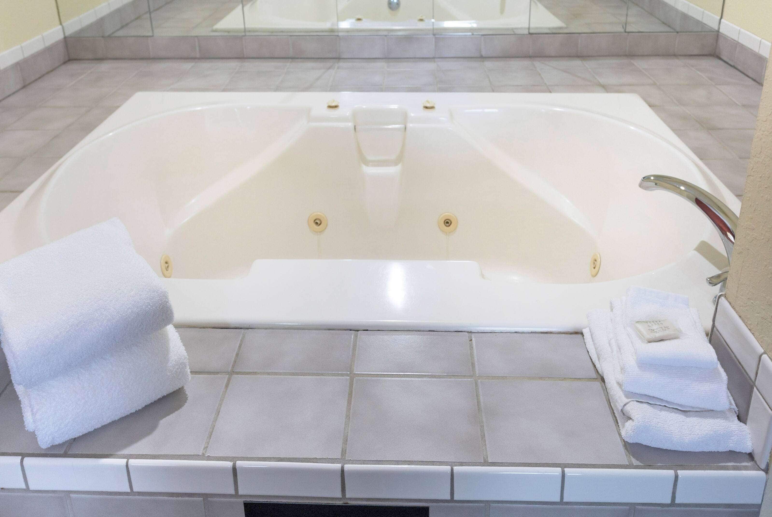 A large, white, freestanding bathtub with a glass-enclosed shower area above it. There are two sets of white towels stacked on the floor beside the tub.