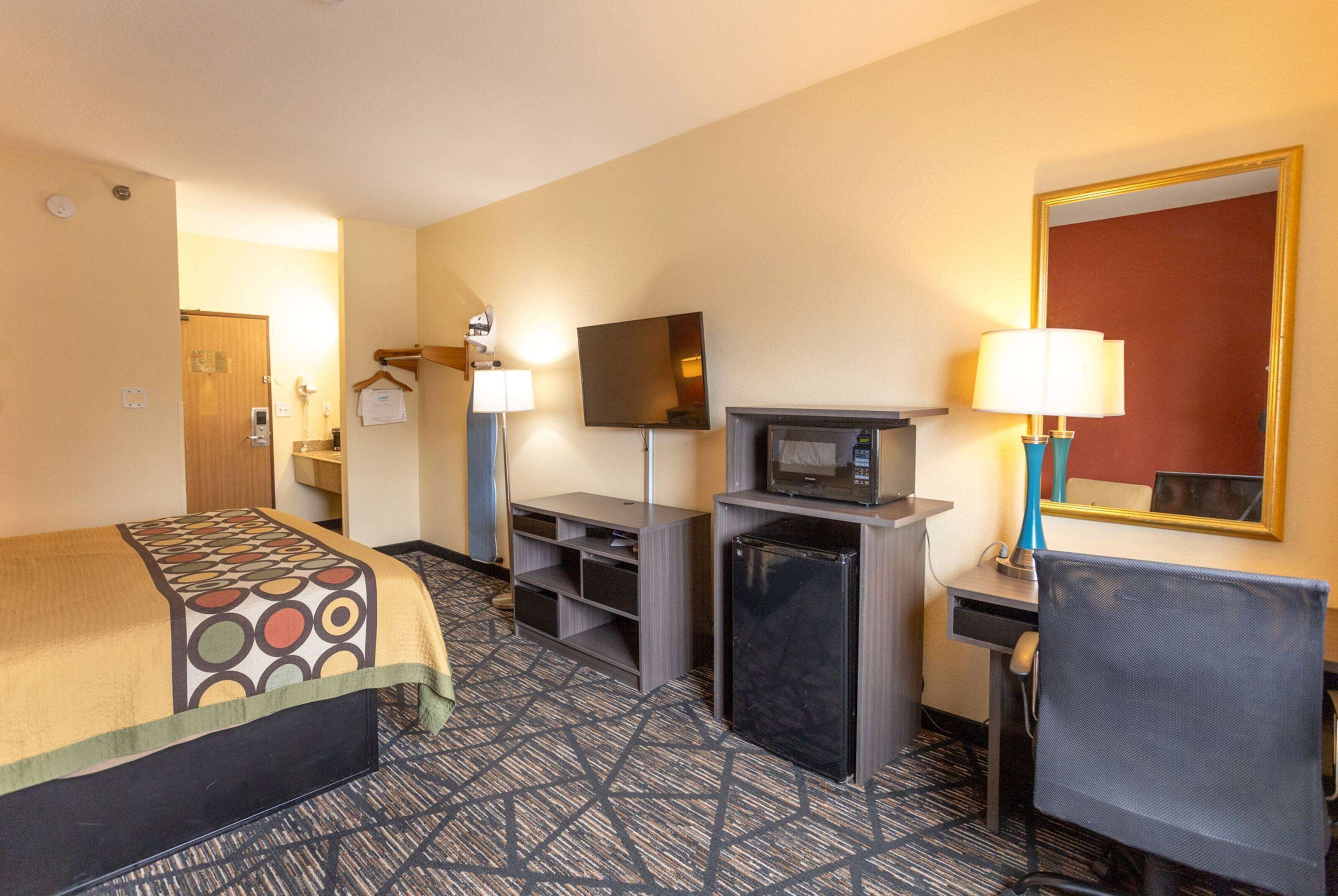 A hotel room with a bed, a desk with a computer, a TV, a microwave, and a chair.