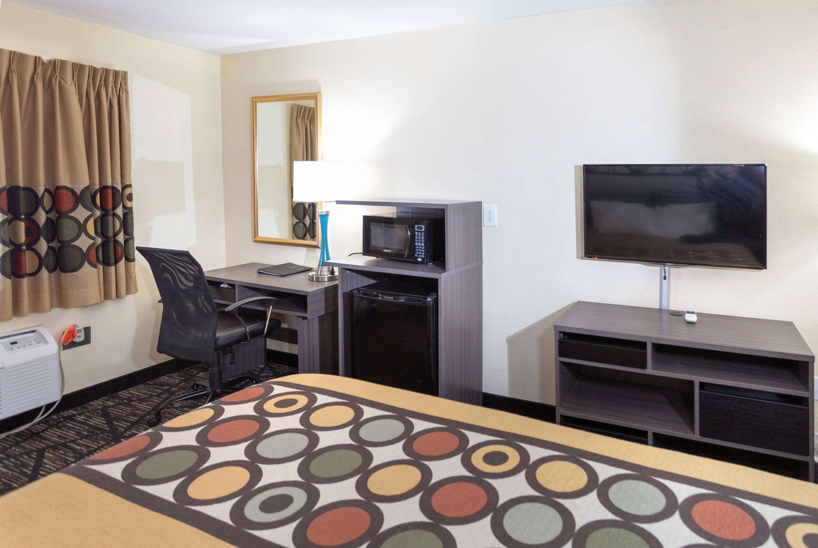 A hotel room with a bed, a desk with a computer, a microwave, a television, and a small refrigerator.